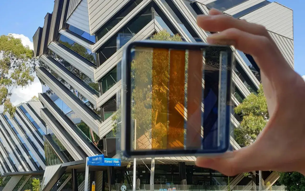 Muestra de cristales fotovoltaicos de colores, reflejando un edificio moderno y árboles.