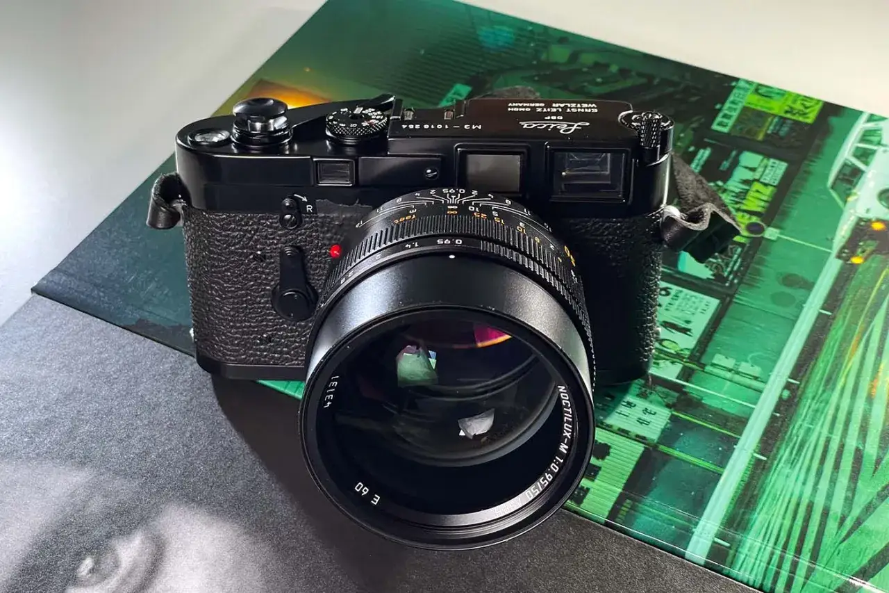 A black Leica M camera with a Noctilux-M 1:0.95/50 lens attached, resting on a green, stylized urban background.