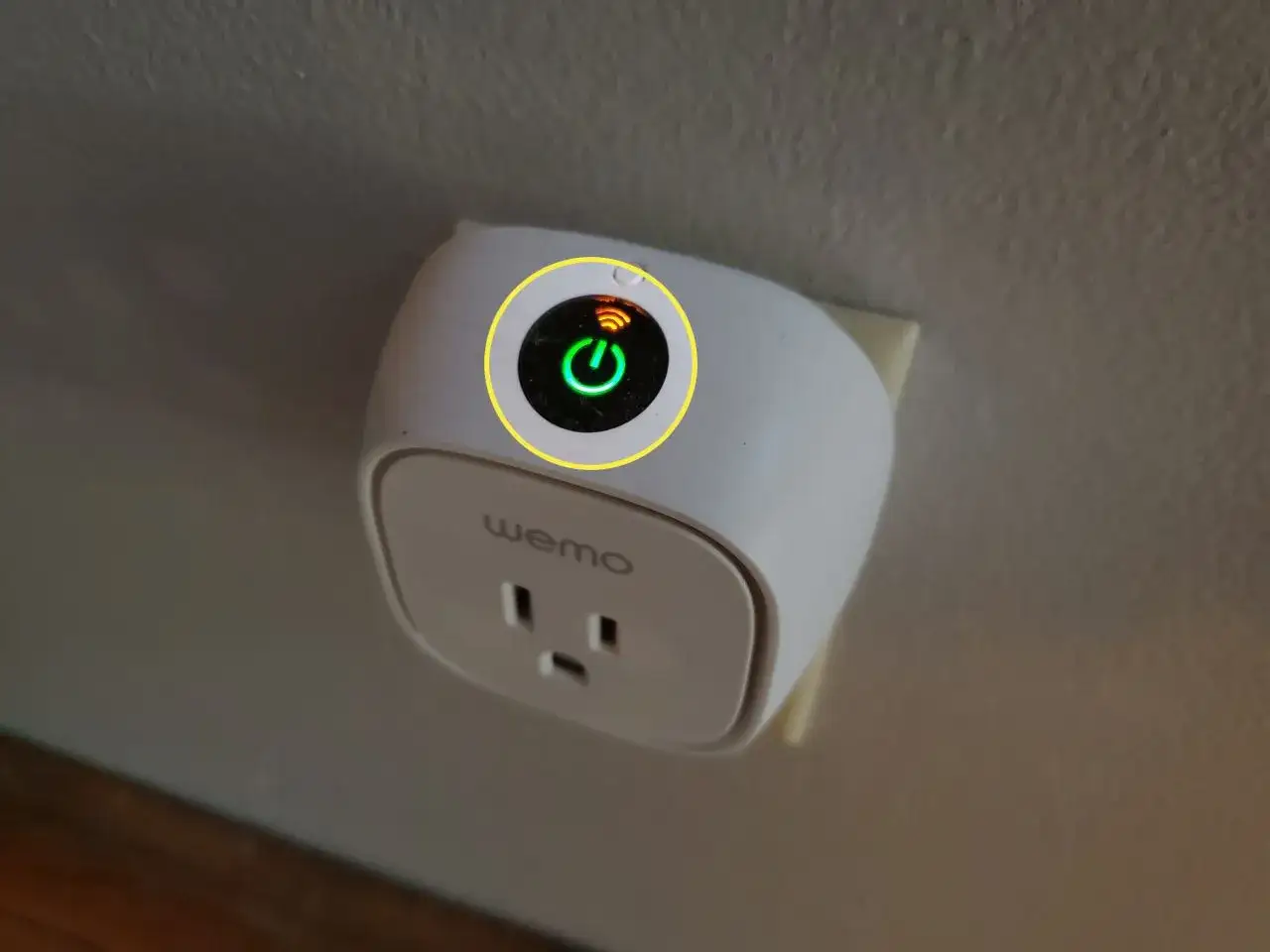 Enchufe inteligente Wemo conectado a la pared, con luz verde de encendido y s&iacute;mbolo de Wi-Fi. Listo para configurar.