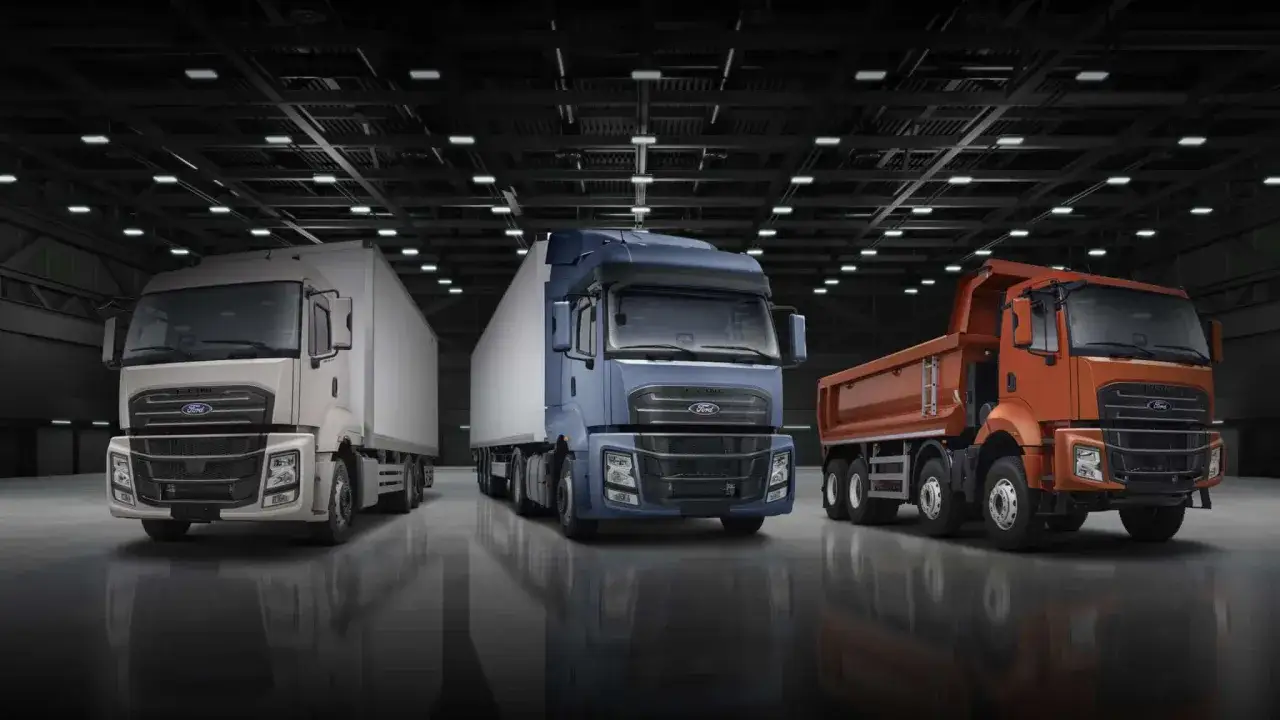 Trois camions Ford F-Line, blanc, bleu et orange, align&eacute;s dans un entrep&ocirc;t.
