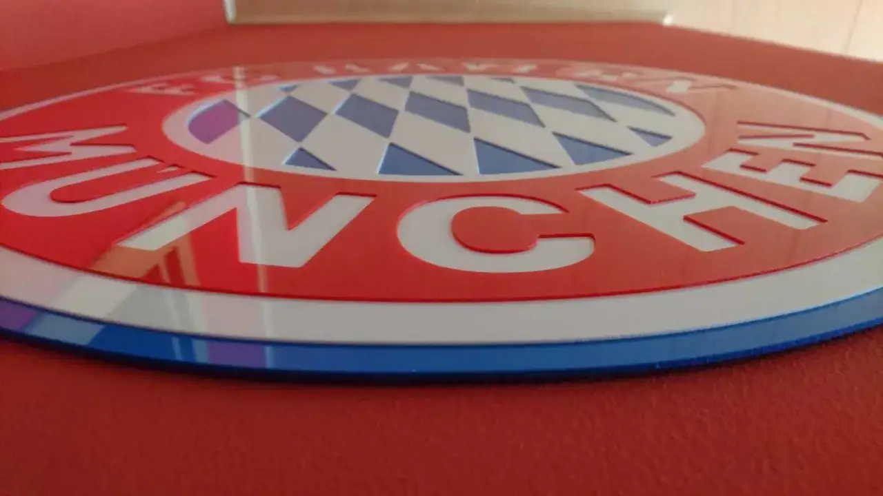 Okrągły, czerwono-biały herb Bayernu Monachium z niebieskimi elementami i charakterystyczną kratką.