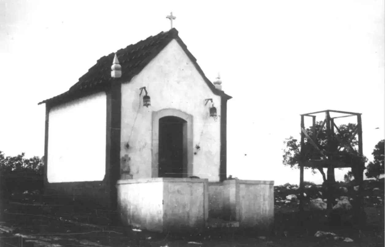 Kaplica w Fatimie, miejsce objawień, z krzyżem na dachu i dzwonkami. Obok widoczna drewniana konstrukcja.