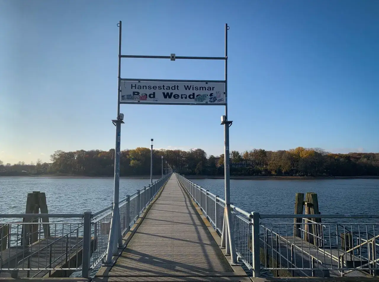 Holzsteg zur Seebr&uuml;cke in Bad Wendorf, Hansestadt Wismar. Ein langer Steg f&uuml;hrt &uuml;ber das ruhige Wasser, ges&auml;umt von Gel&auml;ndern und Laternen.