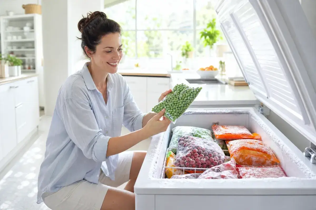 Femme souriante v&eacute;rifiant des petits pois surgel&eacute;s. Elle pourrait ainsi d&eacute;tecter une panne de cong&eacute;lateur si les aliments n'&eacute;taient plus congel&eacute;s.