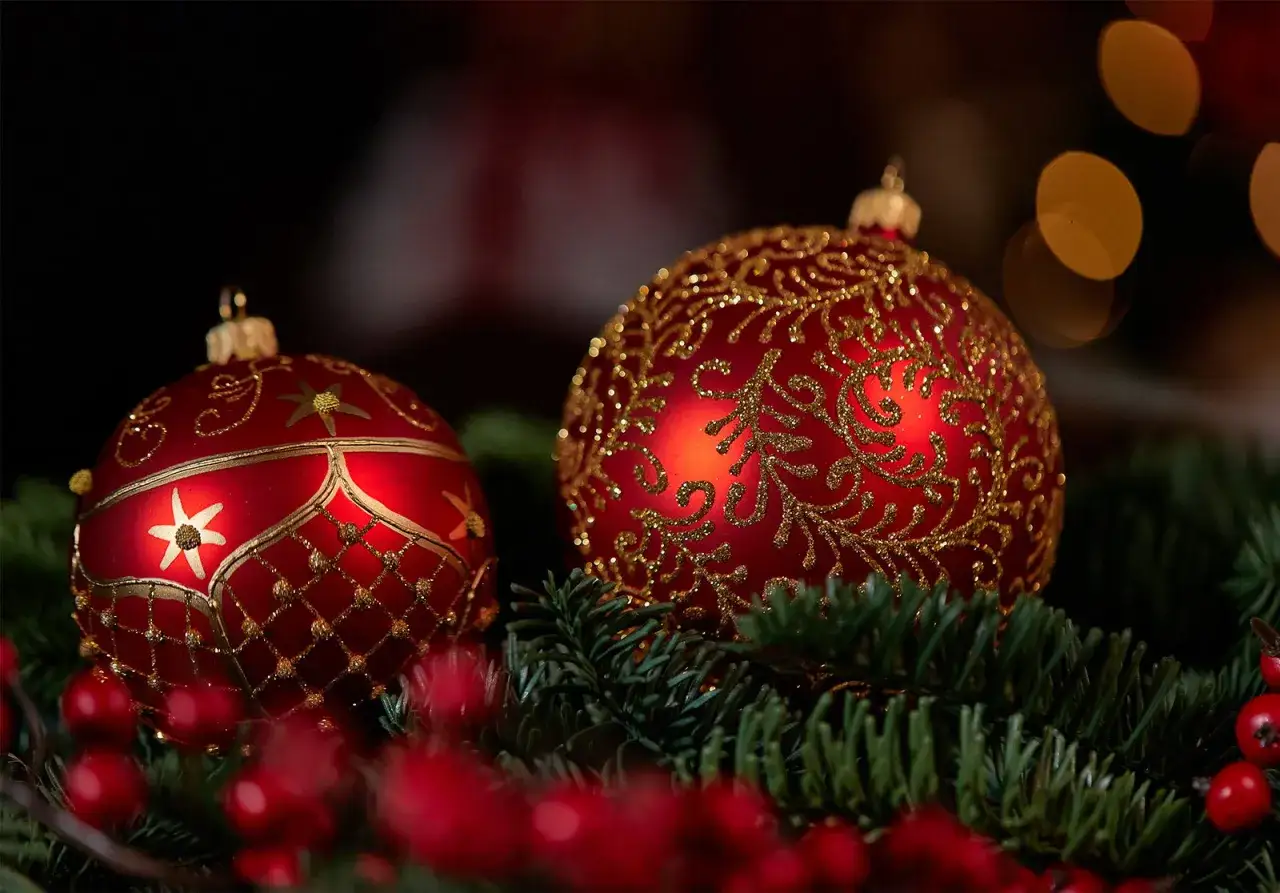 Två röda julgranskulor med gulddetaljer vilar på granris och röda bär. Perfekt julgrans inspo för en lyxig jul.