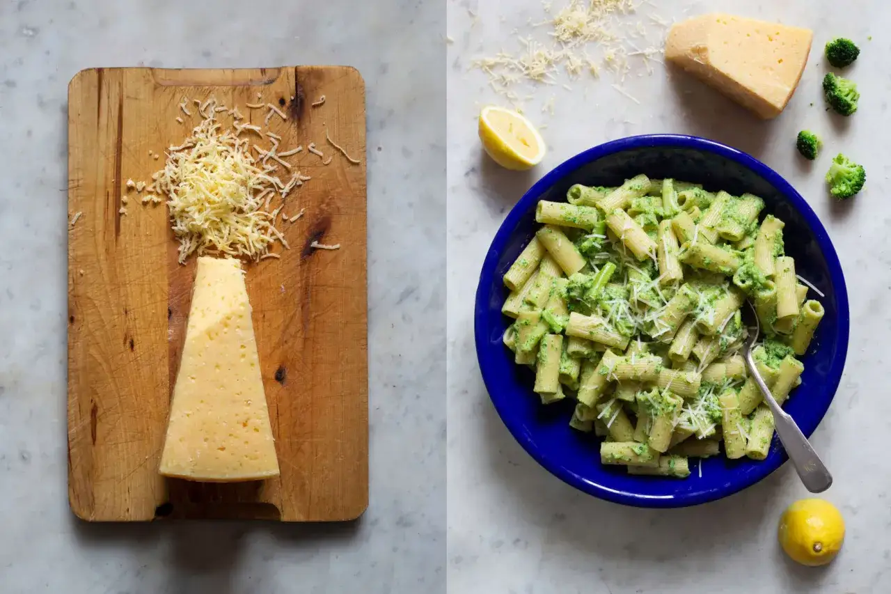 En skål med krämig **broccoli pasta** toppad med riven ost. Bredvid syns en bit ost och en citronklyfta.