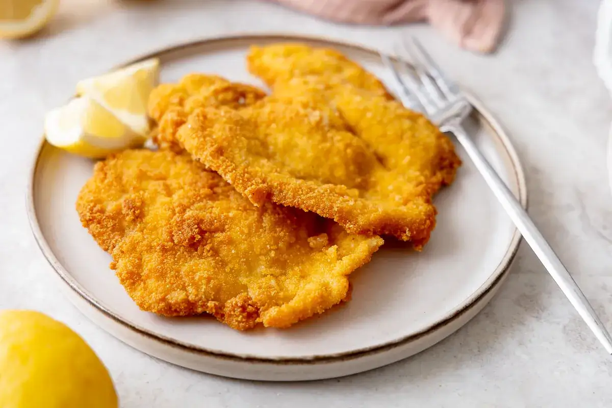 Cotolette dorate e croccanti, perfette cotolette in friggitrice ad aria, servite con spicchi di limone su un piatto.