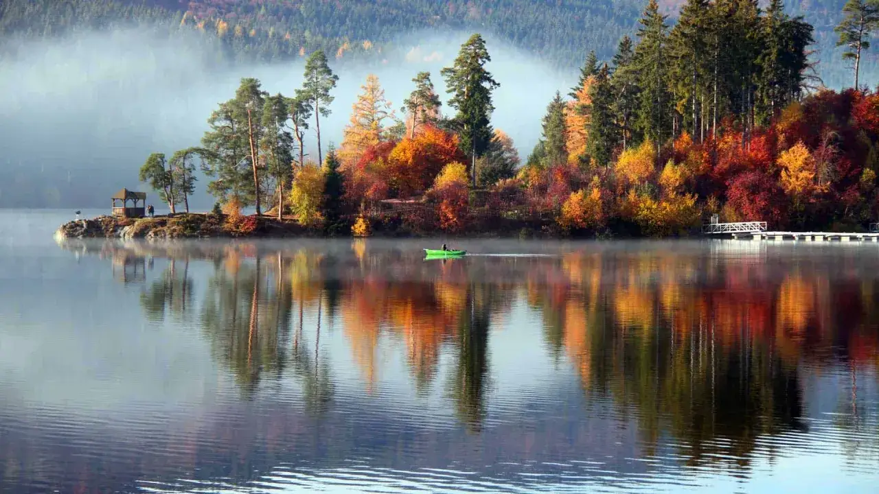 Herbstliche Farben spiegeln sich im See. Ein Boot gleitet durch den Nebel. Perfekte Reiseziele im Oktober in Deutschland.