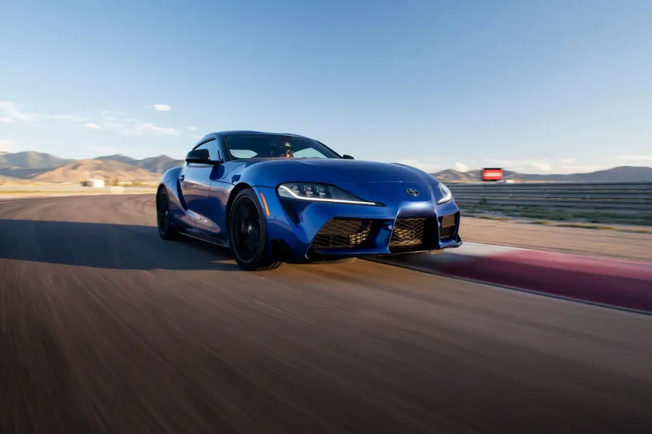 Un BMW Supra azul acelera en una pista de carreras, con monta&ntilde;as al fondo bajo un cielo despejado.