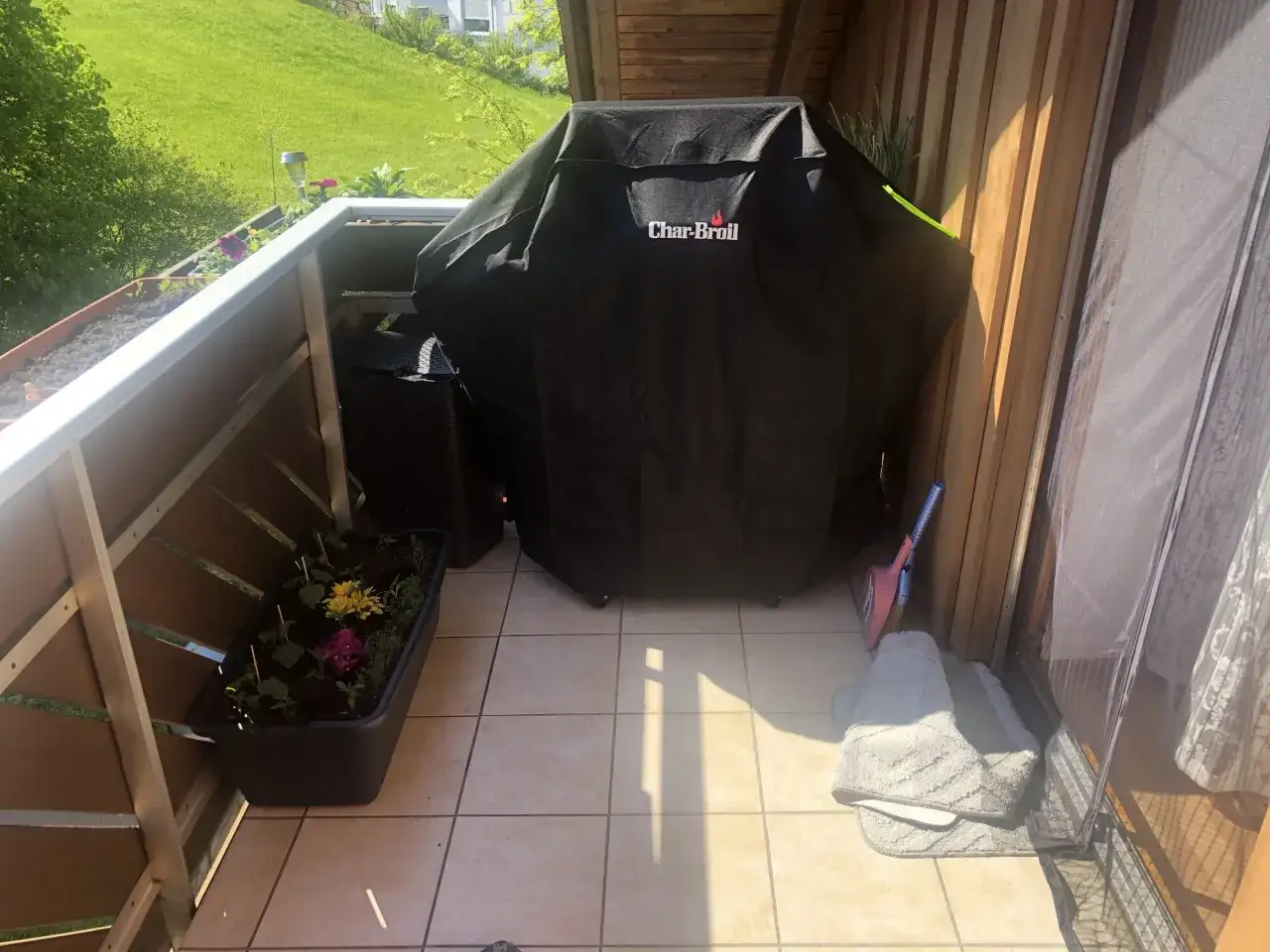 Gasgrill auf dem Balkon, bereit für den Sommer. Blumenkästen und Sonnenschein machen den Balkon zum perfekten Ort.