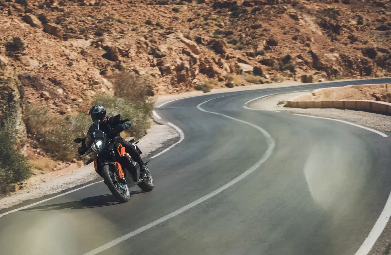 Motociclista en KTM 790 Adventure recorre una carretera sinuosa en un paisaje des&eacute;rtico. Las opiniones sobre esta moto son excelentes para la aventura.