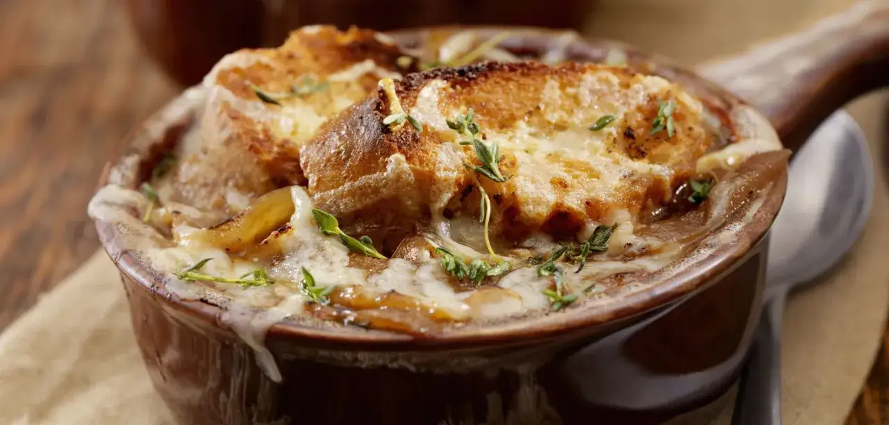 Una ricca zuppa di cipolle toscana, con crostini dorati e formaggio fuso, guarnita con timo fresco.