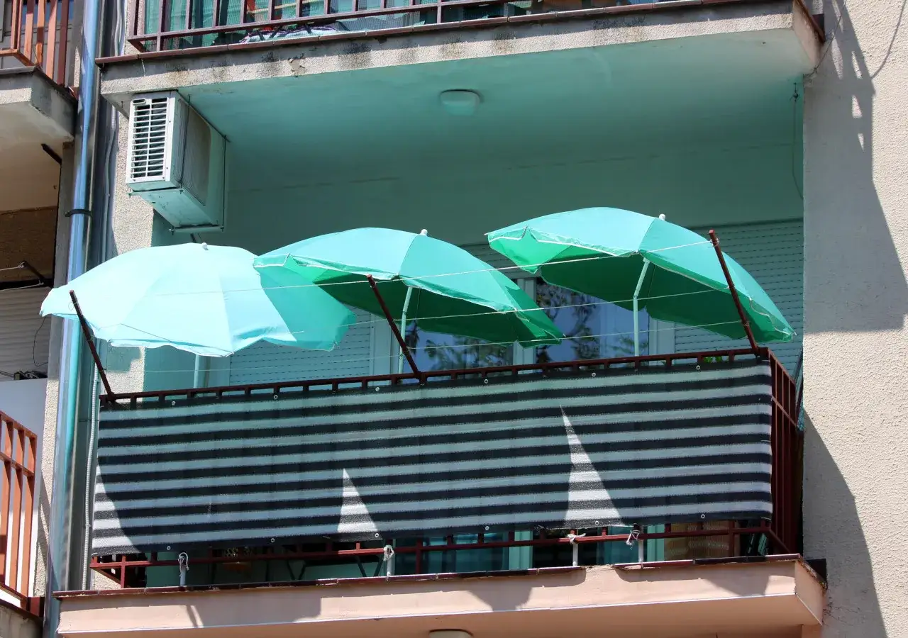 Trzy parasole tworzą zacienienie, pokazując, jak osłonić balkon przed słońcem. Siatka na balustradzie dodatkowo chroni przed wiatrem i ciekawskimi spojrzeniami.