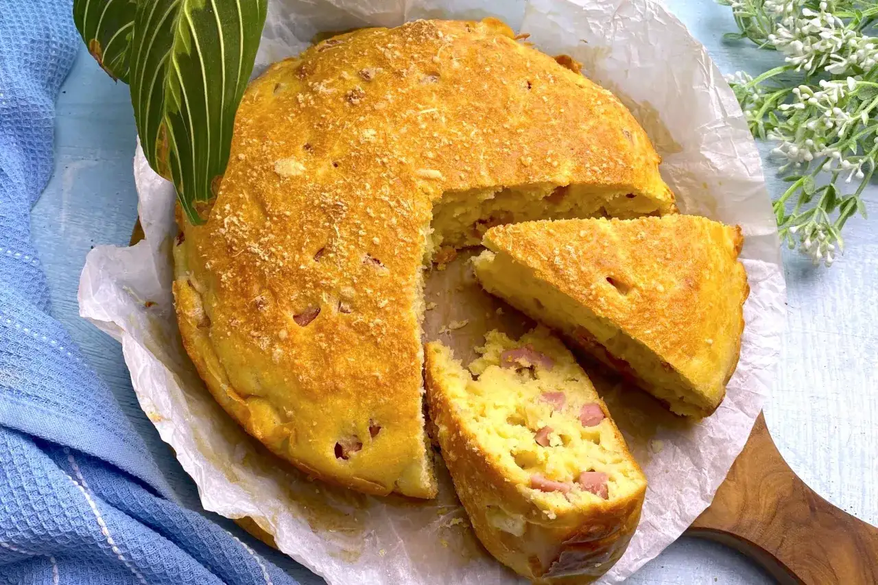Torta salata prosciutto e formaggio, dorata e fragrante, con una fetta tagliata che rivela cubetti di prosciutto e formaggio filante.