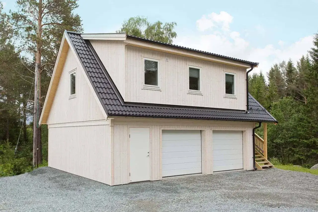 Ett modernt garage med tv&aring; portar och en d&ouml;rr, redo att bygga om till bostad. Omgiven av skog.