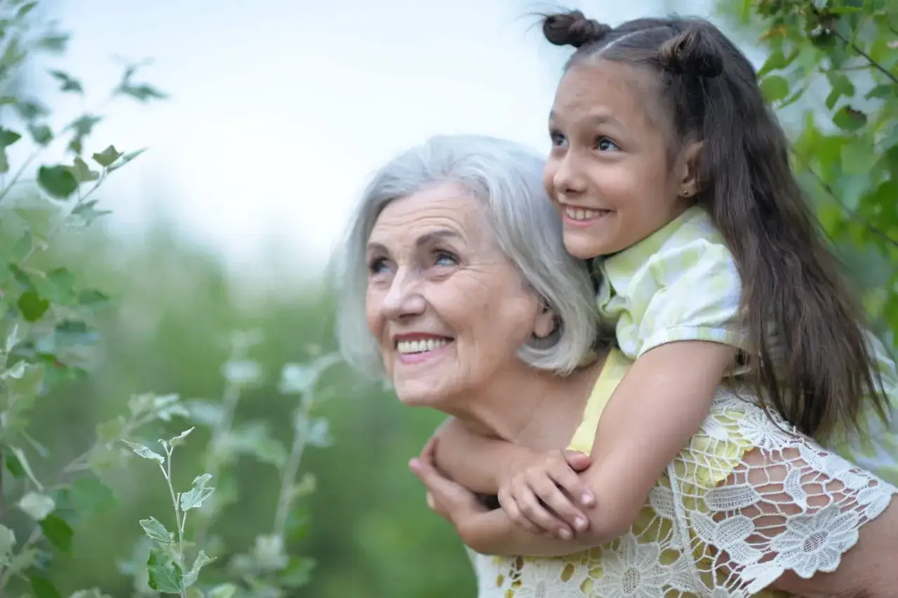 Une petite fille fait un gros câlin à sa grand-mère indifférente, toutes deux regardant vers le ciel avec des sourires radieux.