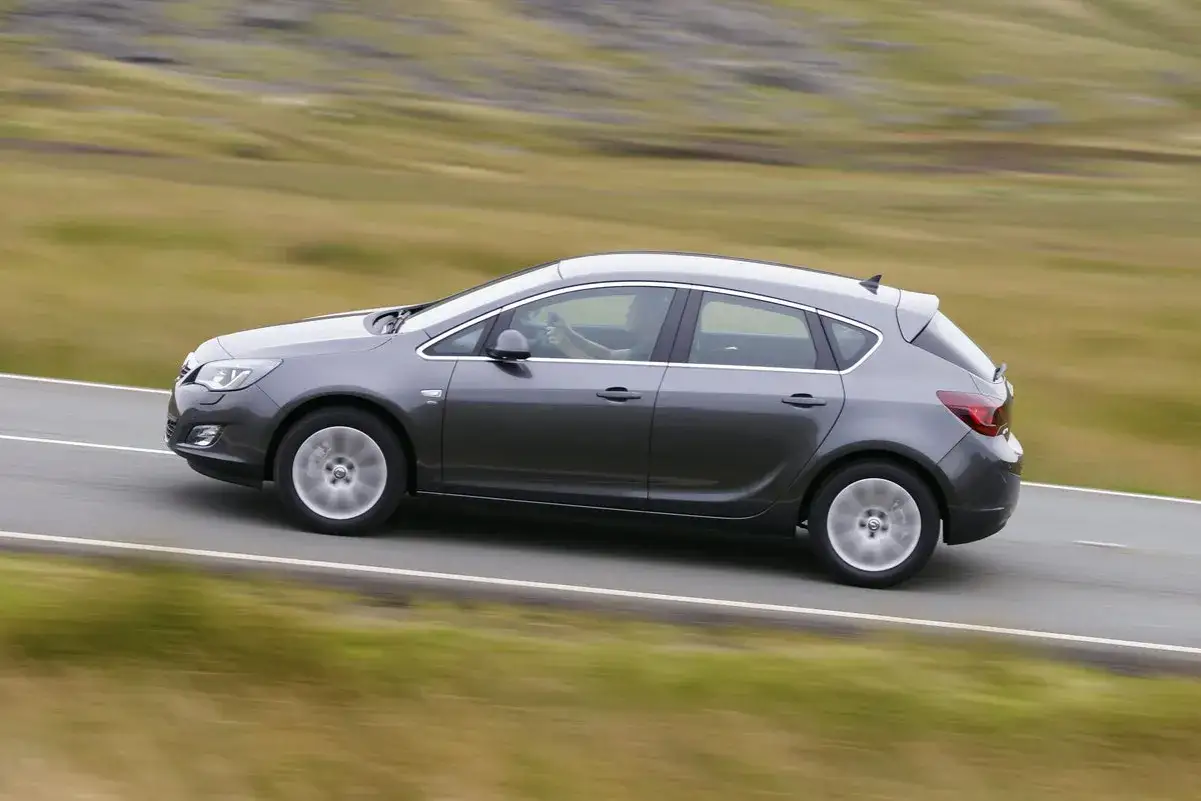 Gr&aring; Opel Astra 2016 k&ouml;r p&aring; en landsv&auml;g. En f&ouml;rare syns bakom ratten.
