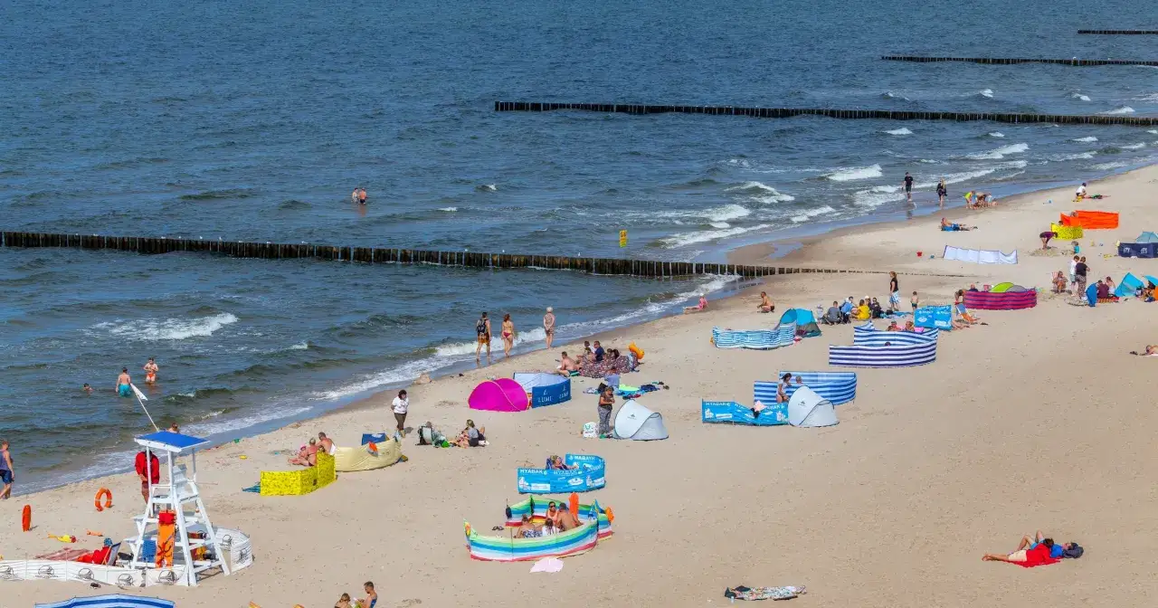 Plaża pełna ludzi, gdzie jest najcieplejsze morze w Polsce? Woda przy brzegu jest spokojna, a fale delikatnie rozbijają się o piasek.
