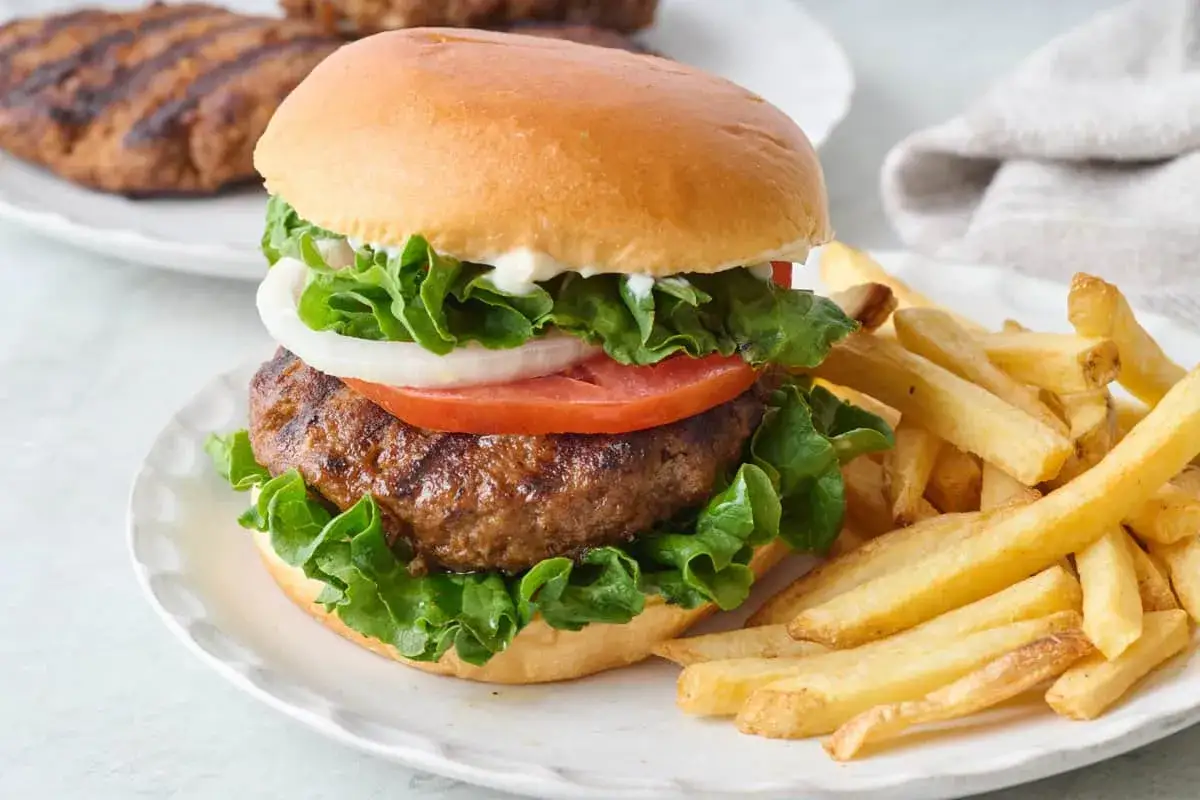 McRoyal makro: soczysty burger z sałatą, pomidorem i cebulą, podany z chrupiącymi frytkami na talerzu.