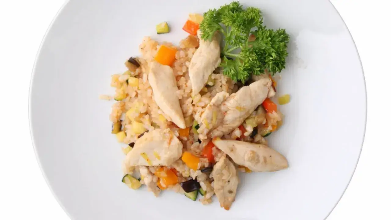 Un piatto di riso con pollo e verdure miste, guarnito con prezzemolo fresco. Un pasto leggero e gustoso.