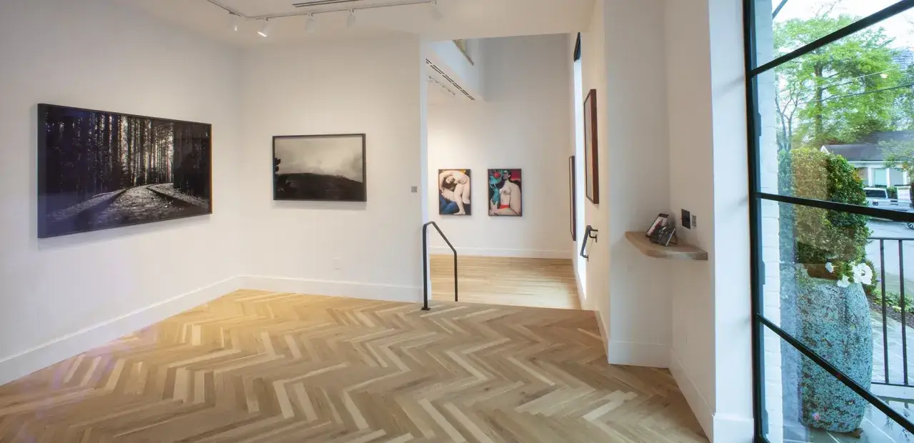 Inside Jackson Fine Art Atlanta, a gallery with herringbone wood floors, featuring striking photography of a forest path, a misty landscape, and figurative art.