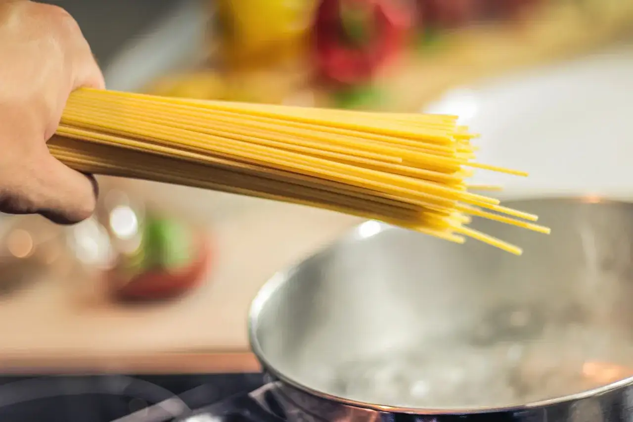 Hand h&auml;lt Spaghetti &uuml;ber kochendes Wasser. So einfach ist es, wie koche ich nudeln.