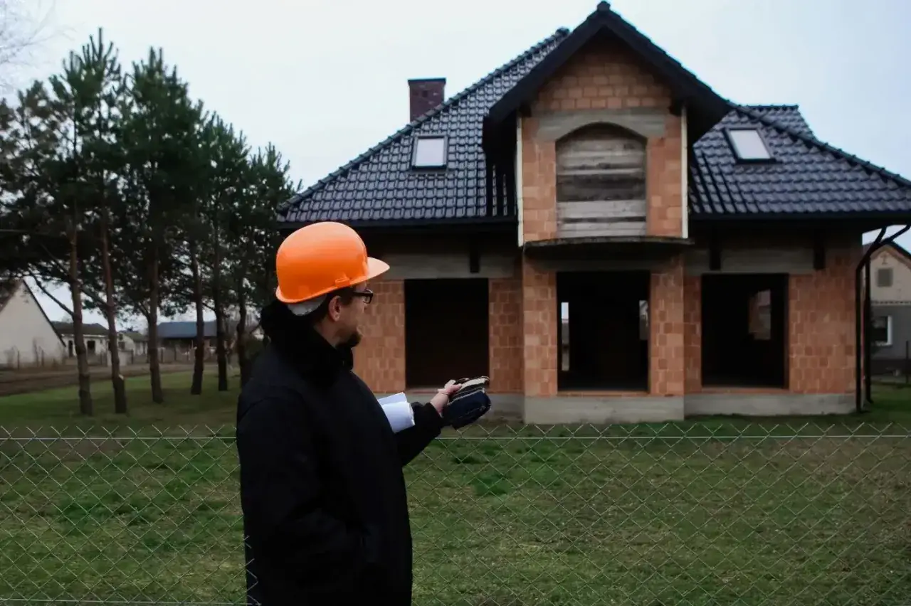 Inżynier w kasku ogląda budynek mieszkalny jednorodzinny w stanie surowym.