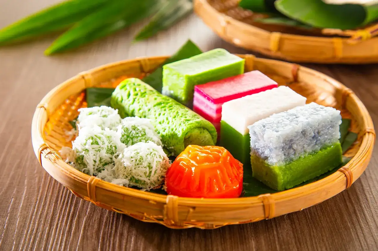 Bunte asiatische Nachspeisen wie gr&uuml;ne R&ouml;llchen, Kokoskugeln und Schichtkuchen in einem Korbe.