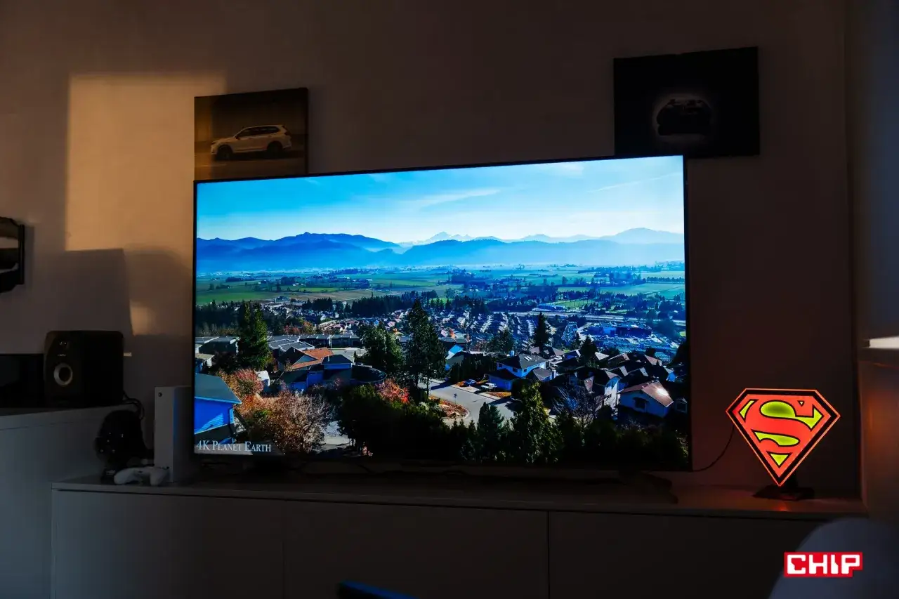 Telewizor TCL C655 wyświetla krajobraz z lotu ptaka. Obok stoi lampka z symbolem Supermana.