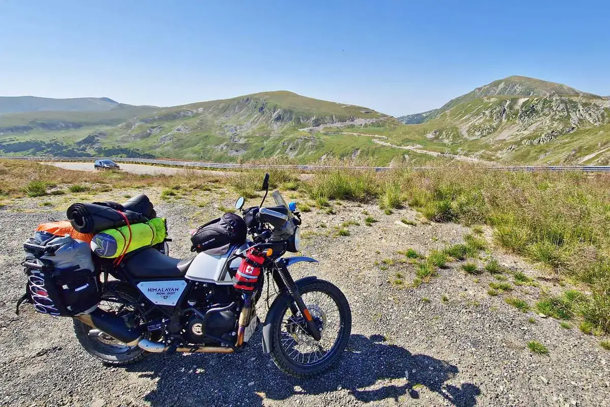 Motocykl z bagażem na tle górskiej drogi w Rumunii. Podróż motocyklem po Rumunii, koszty takiej wyprawy są różne.