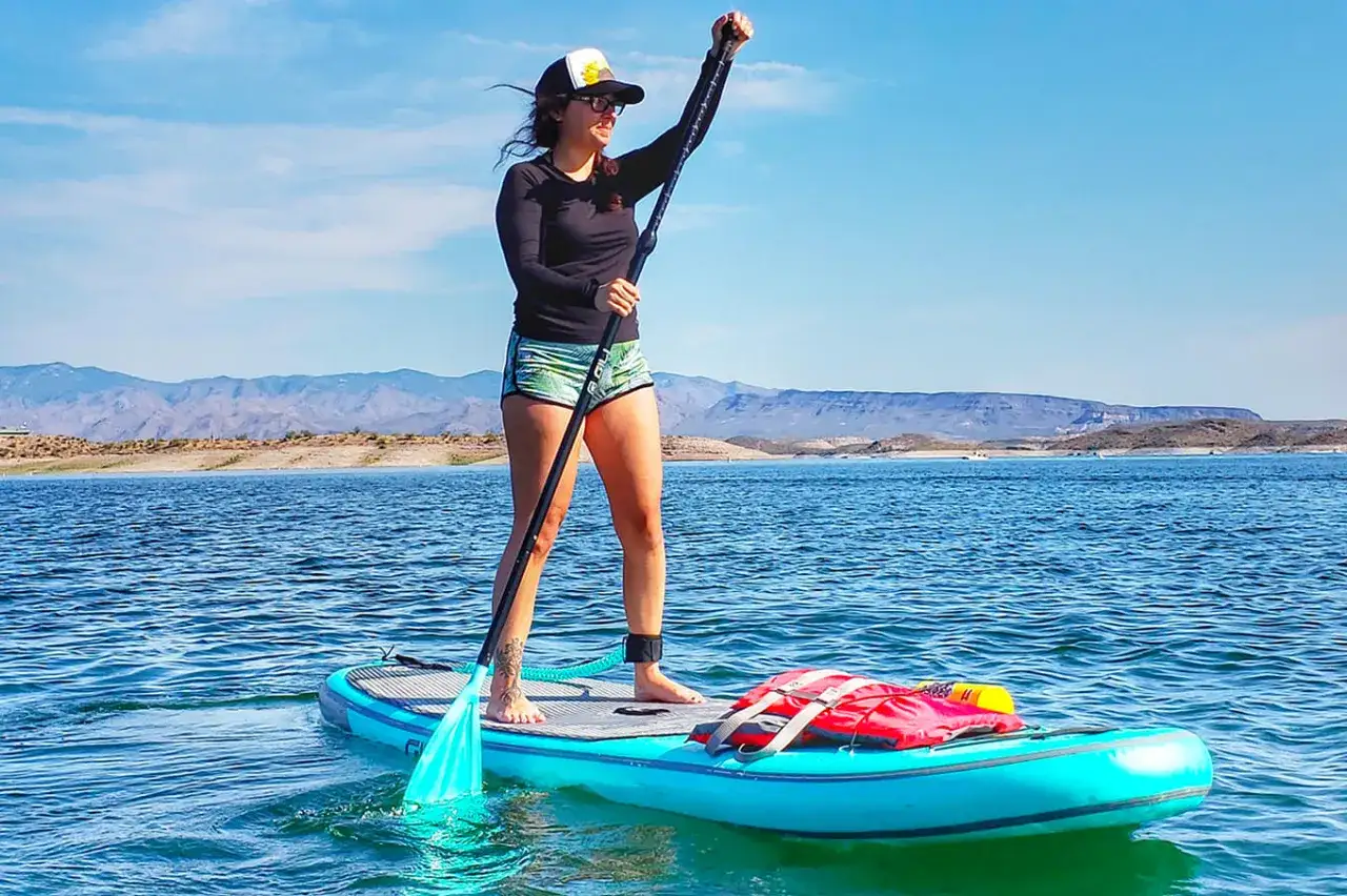 Donna in piedi su una tavola da sup, pagaia in mano, con montagne sullo sfondo. Ecco come si usa il sup!