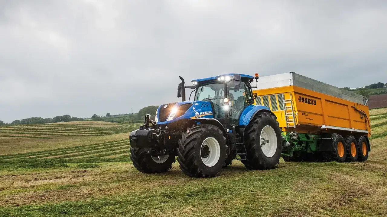 Un tracteur bleu New Holland, c'est quoi ? C'est ce puissant engin qui tracte une remorque jaune dans un champ fauch&eacute;.