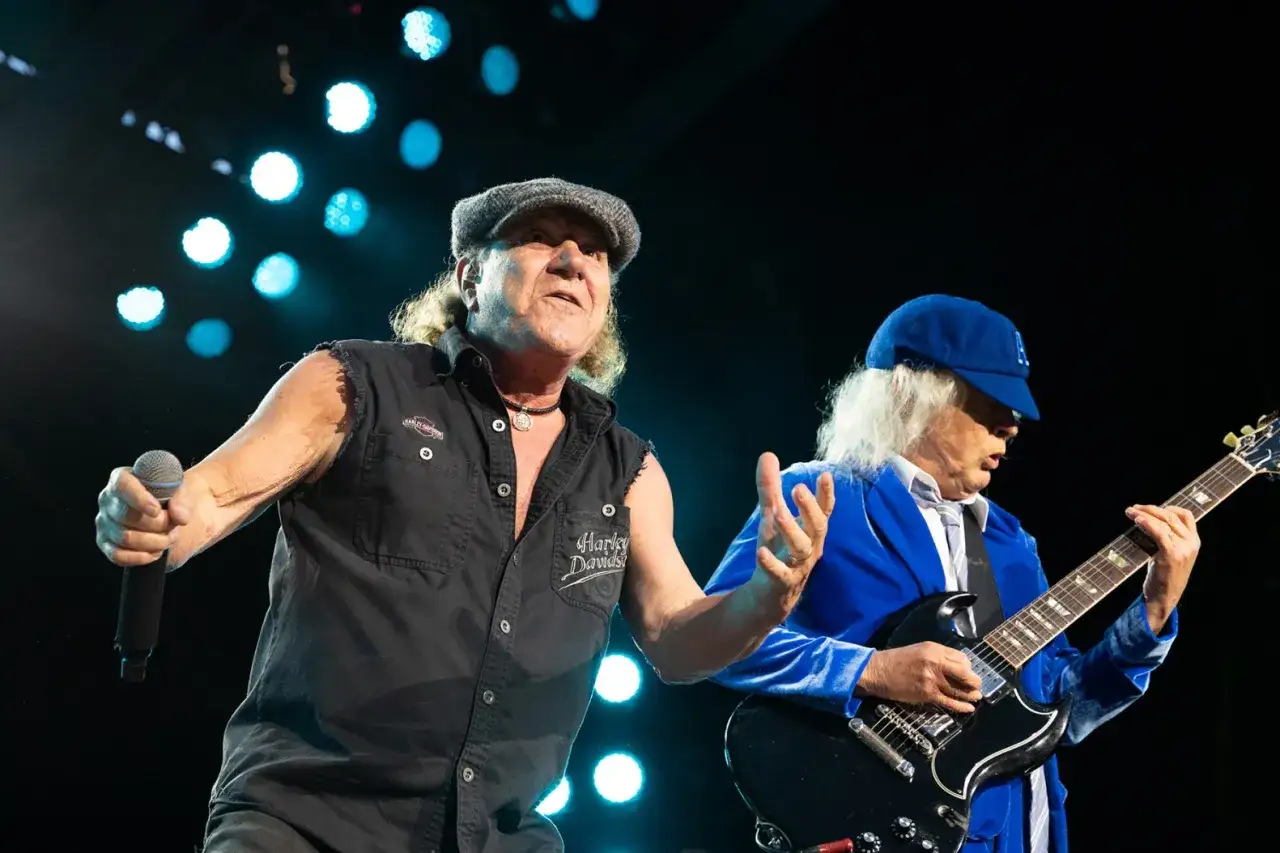 Wokalista i gitarzysta zespołu AC/DC na scenie. Brian Johnson w czapce i koszuli bez rękawów, Angus Young w niebieskiej marynarce i czapce.