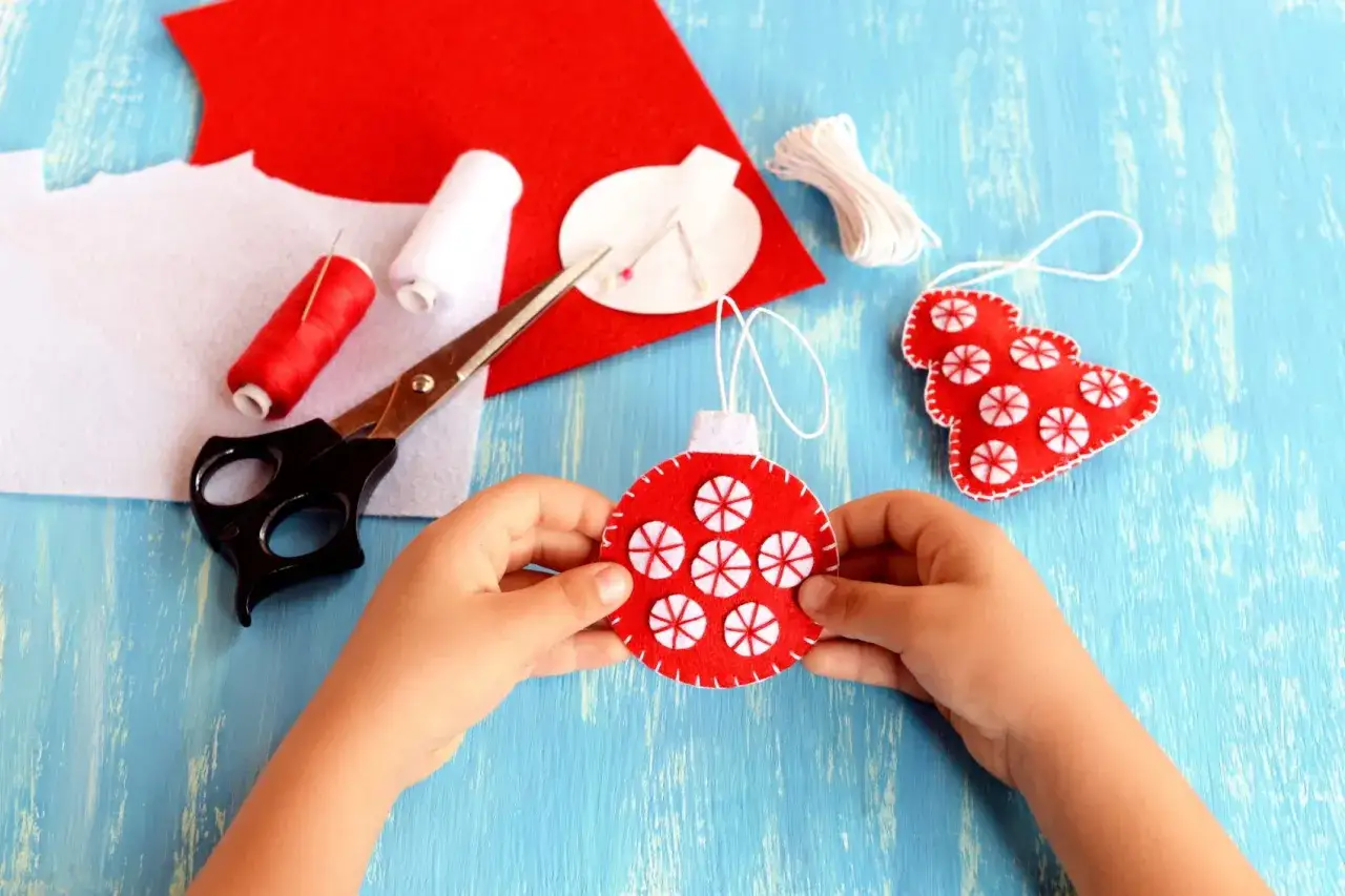 Bambino crea decorazioni natalizie con feltro rosso e bianco, ago e filo. Lavoretti con ago e filo per bambini, perfetti per le feste.
