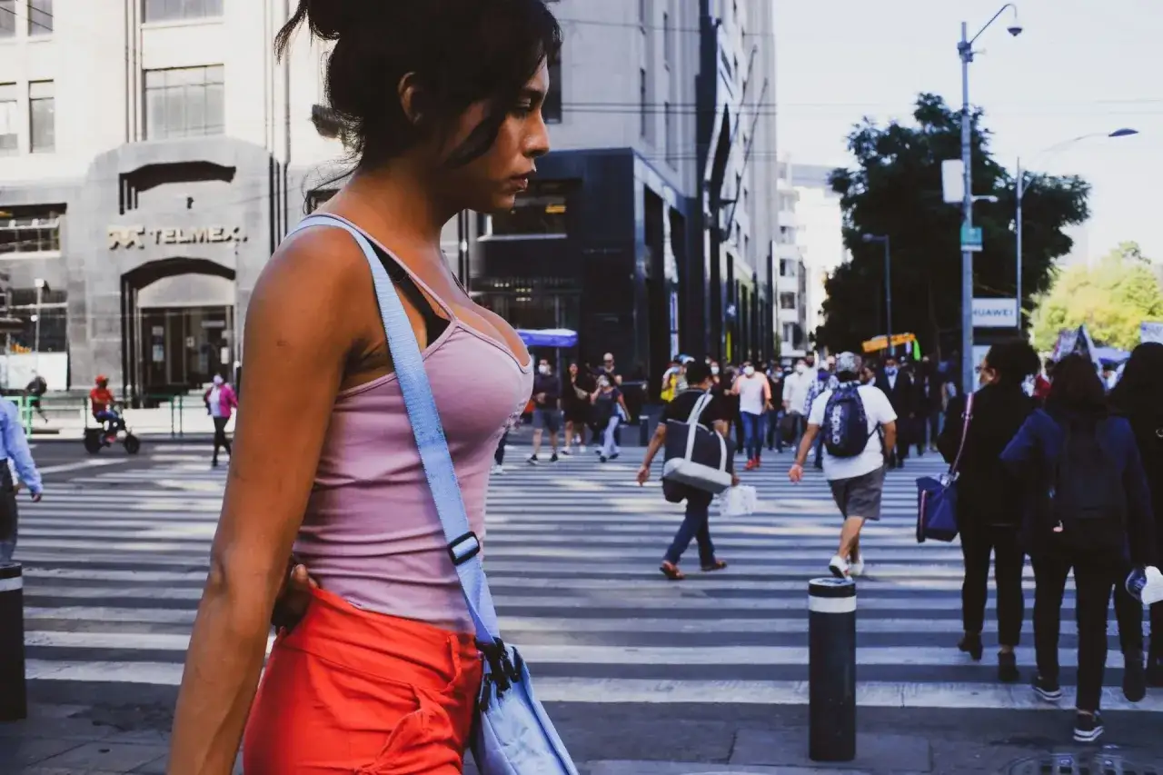 A woman in a pink tank top and orange shorts walks across a busy street, a perfect subject for street photography.