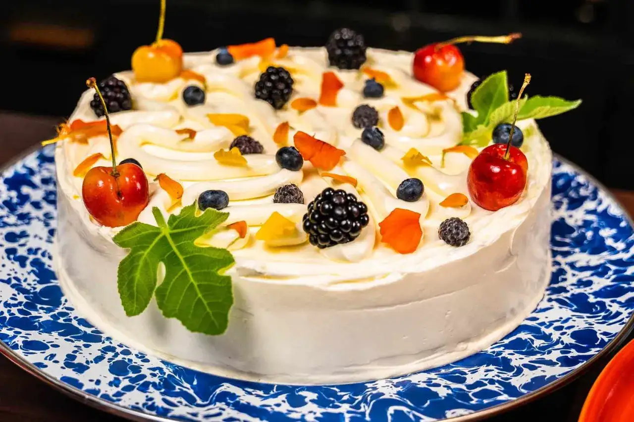 Ein wunderschöner Kuchen zum Muttertag, verziert mit Sahne, Kirschen, Brombeeren, Blaubeeren und einem Feigenblatt.