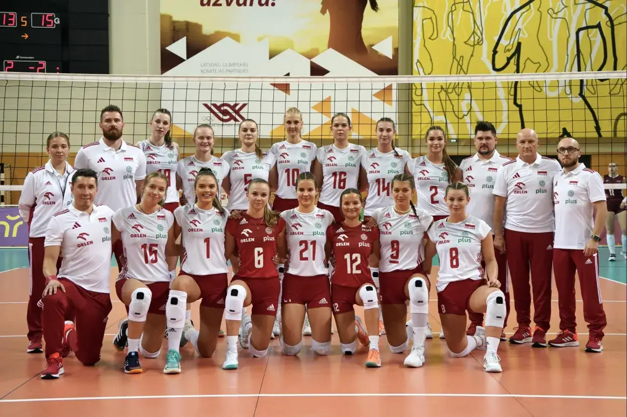 Drużyna siatkarska u 21 w białych strojach z czerwonymi detalami, pozuje do zdjęcia.