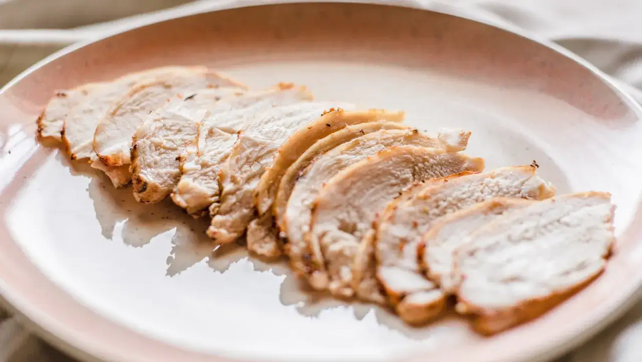 Lonchas de fiambre de pollo casero, jugosas y doradas, servidas en un plato rosa.
