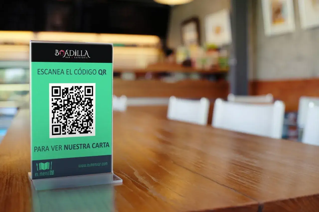 En la mesa de un bar, un letrero verde invita a escanear un c&oacute;digo QR para ver la carta digital.
