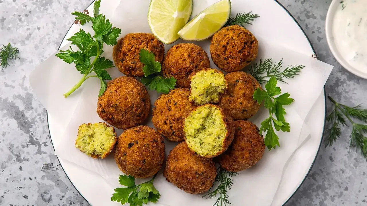 Knusprige Falafelbällchen, die aus Kichererbsen, Kräutern und Gewürzen bestehen, garniert mit Petersilie und Limettenspalten.