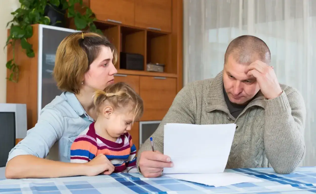 Rodzina przy stole analizuje dokumenty. Czy to rachunki, czy może wnioski o babciowe dla kogoś?