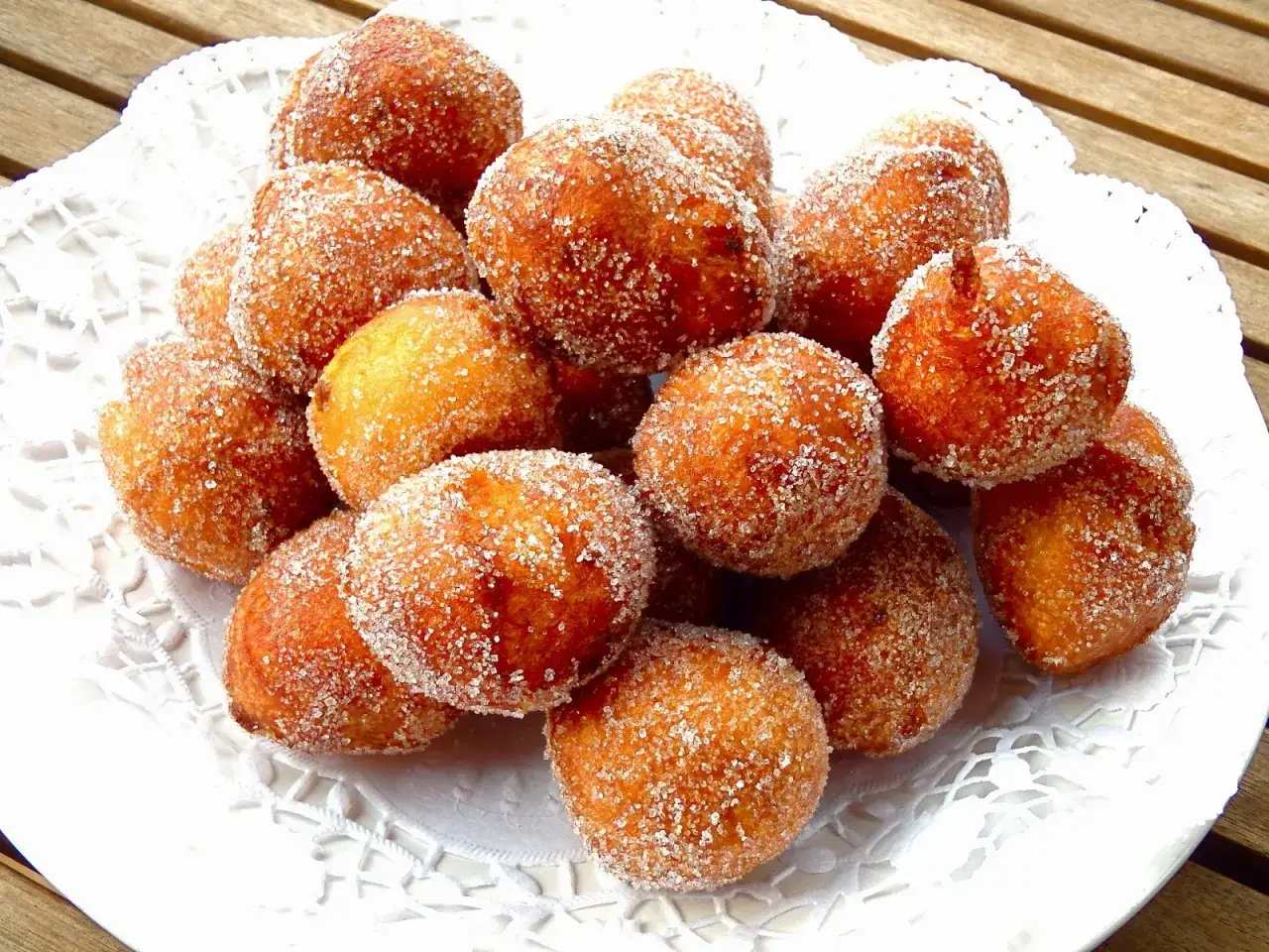 Montón de buñuelos de cuaresma dorados y espolvoreados con azúcar, servidos en un plato blanco con encaje.