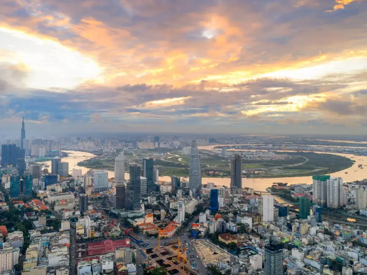 Ho Chi Minh Miasto o zachodzie słońca. Chmury malują niebo na pomarańczowo nad rozległą panoramą miasta z rzeką i drapaczami chmur.