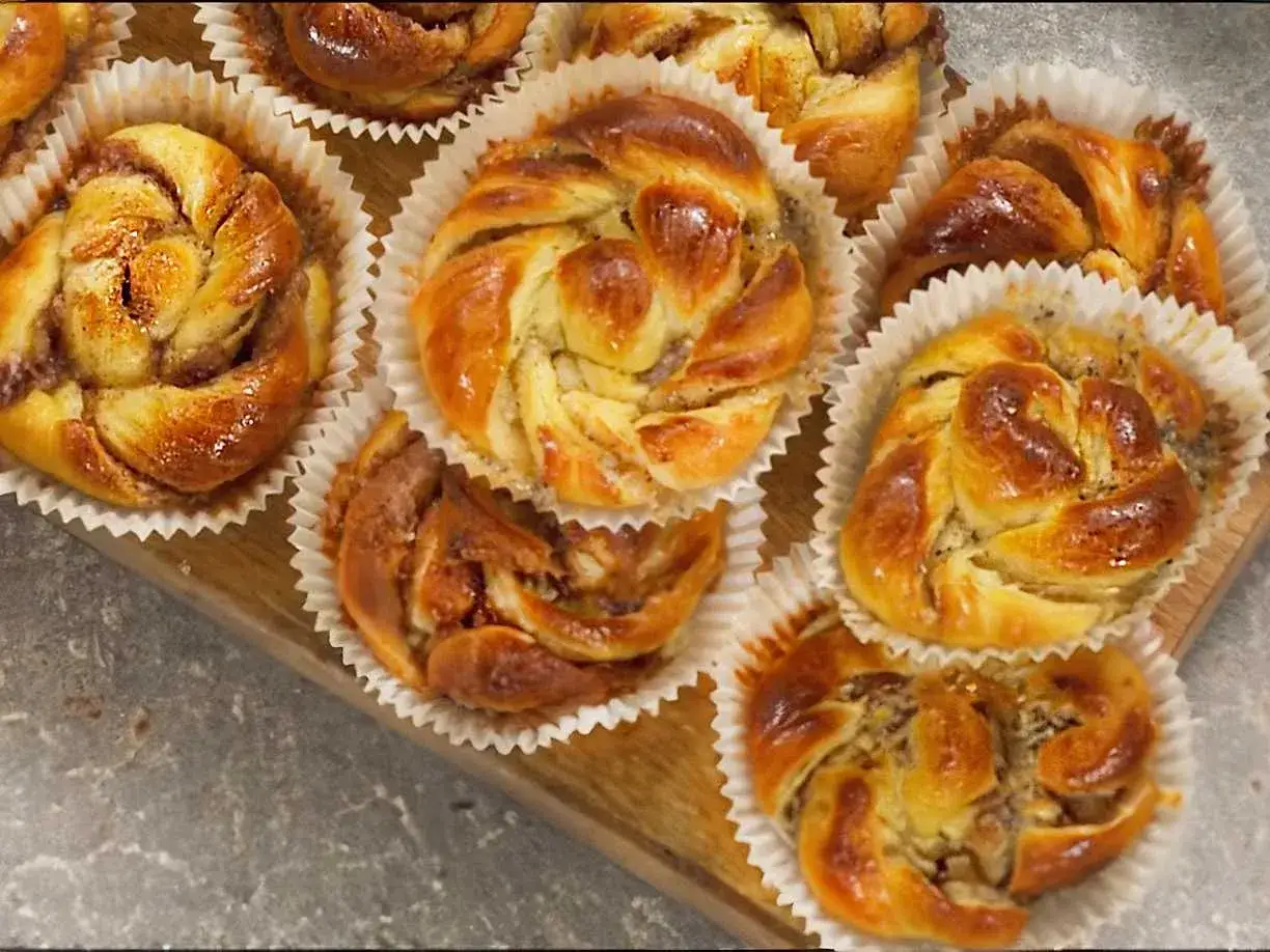 Nybakade bullar med mandelmassa, kanel och vallmofrön i pappersformar på en träbricka.