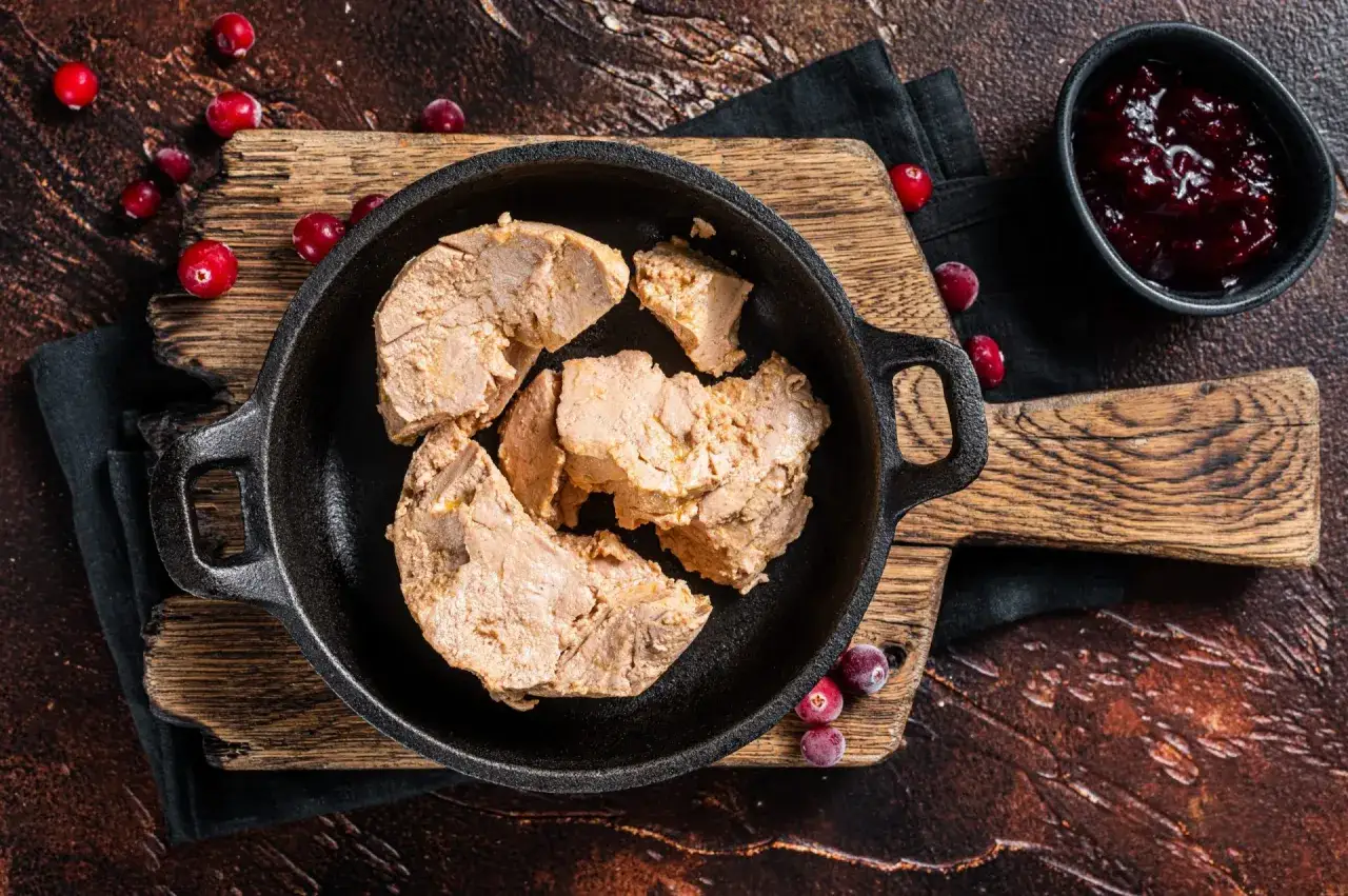 Morceaux de foie gras dans une po&ecirc;le en fonte, pr&ecirc;ts &agrave; assaisonner. Des airelles rouges et une compote de fruits accompagnent ce d&eacute;lice.