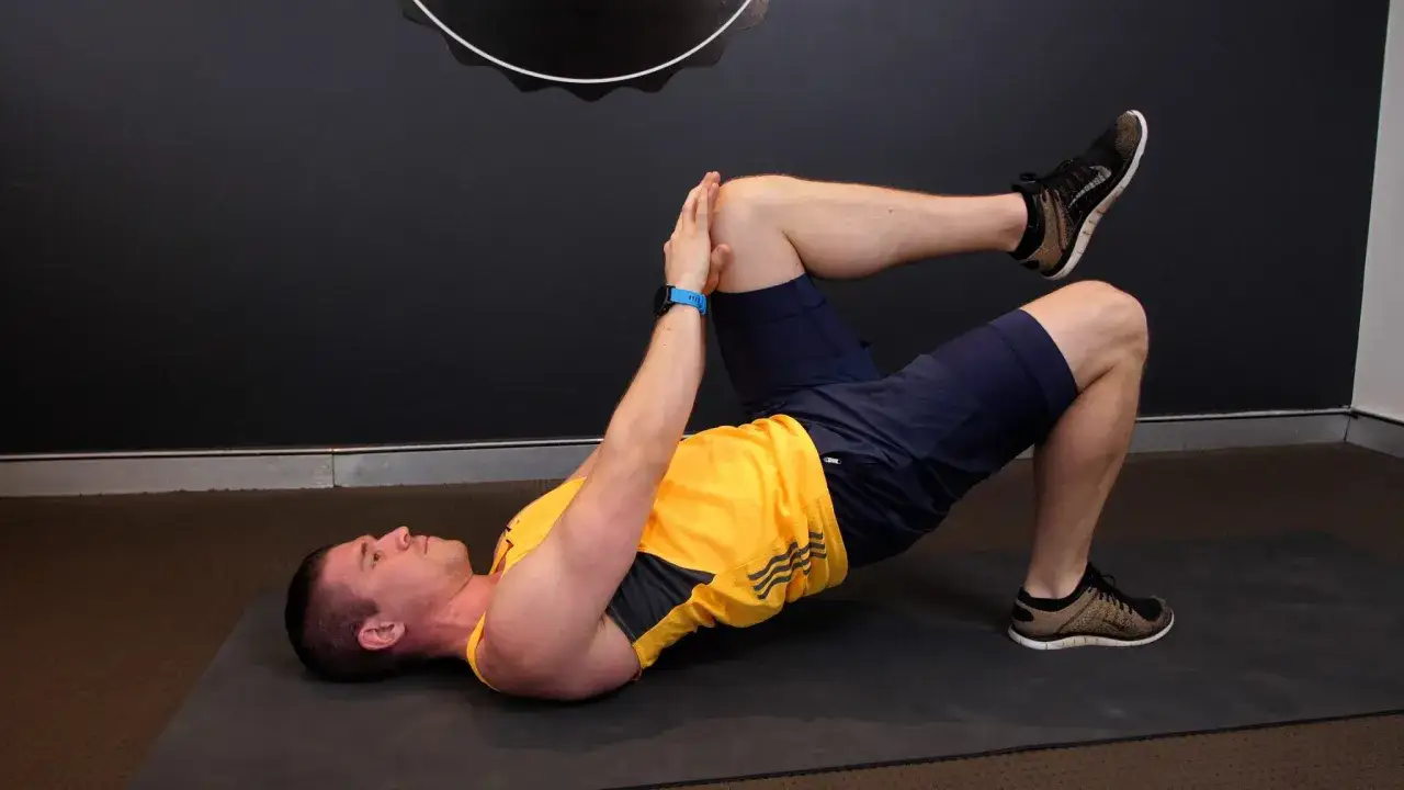 Mężczyzna wykonuje ćwiczenie na macie, unosząc biodra w górę. To ćwiczenie wzmacnia mięśnie pośladków i poprawia **hip extension**.