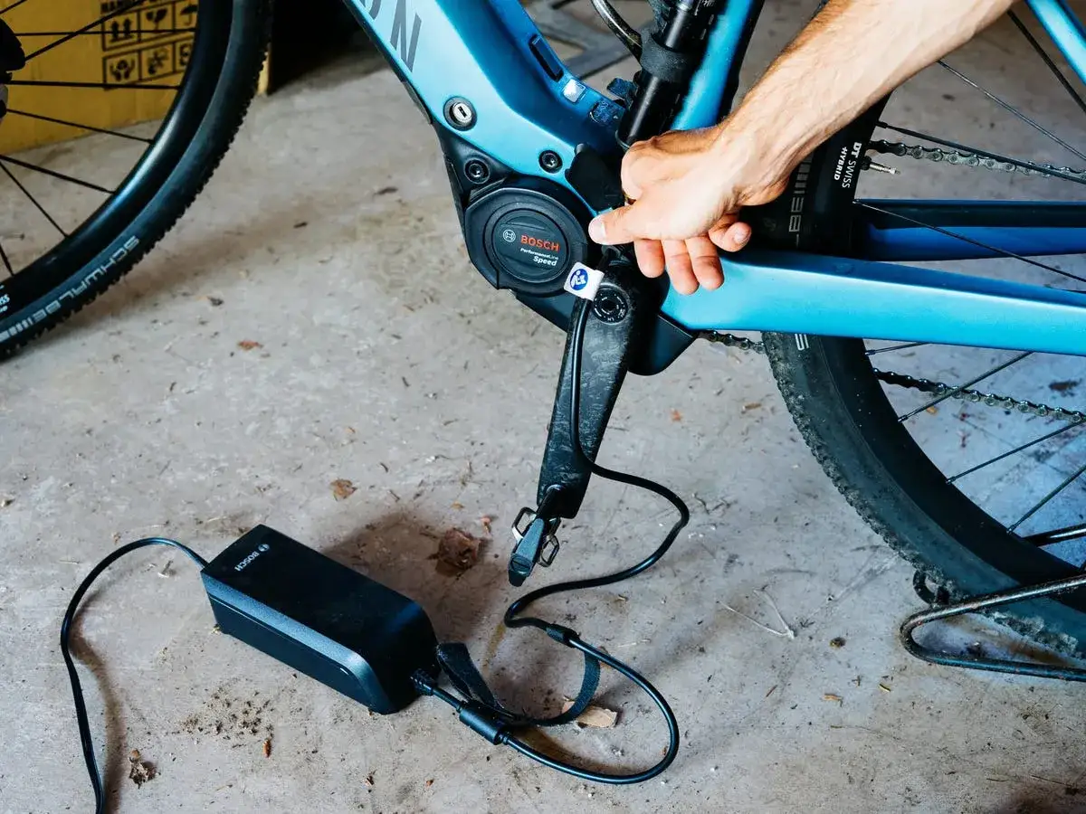 Pierwsze ładowanie baterii rowerowej Bosch. Ręka podłącza ładowarkę do silnika roweru elektrycznego.