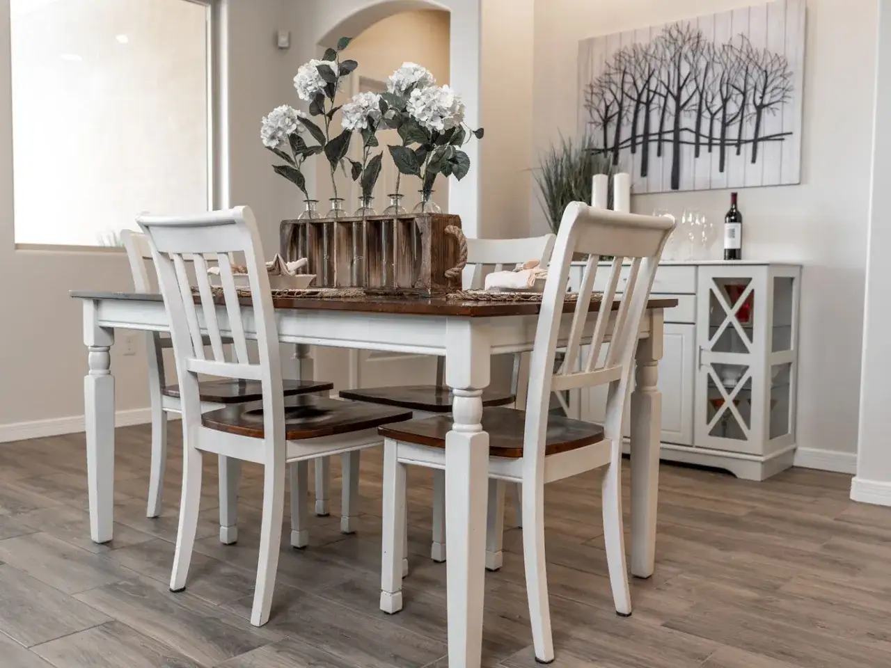 Urocze wnętrza w stylu shabby chic: drewniany st&oacute;ł z białymi krzesłami, bukiet białych hortensji w szklanych wazonach.