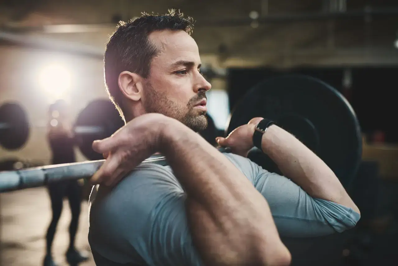 Mann hebt Langhantel im Fitnessstudio. Vitamin D unterst&uuml;tzt den Muskelaufbau.