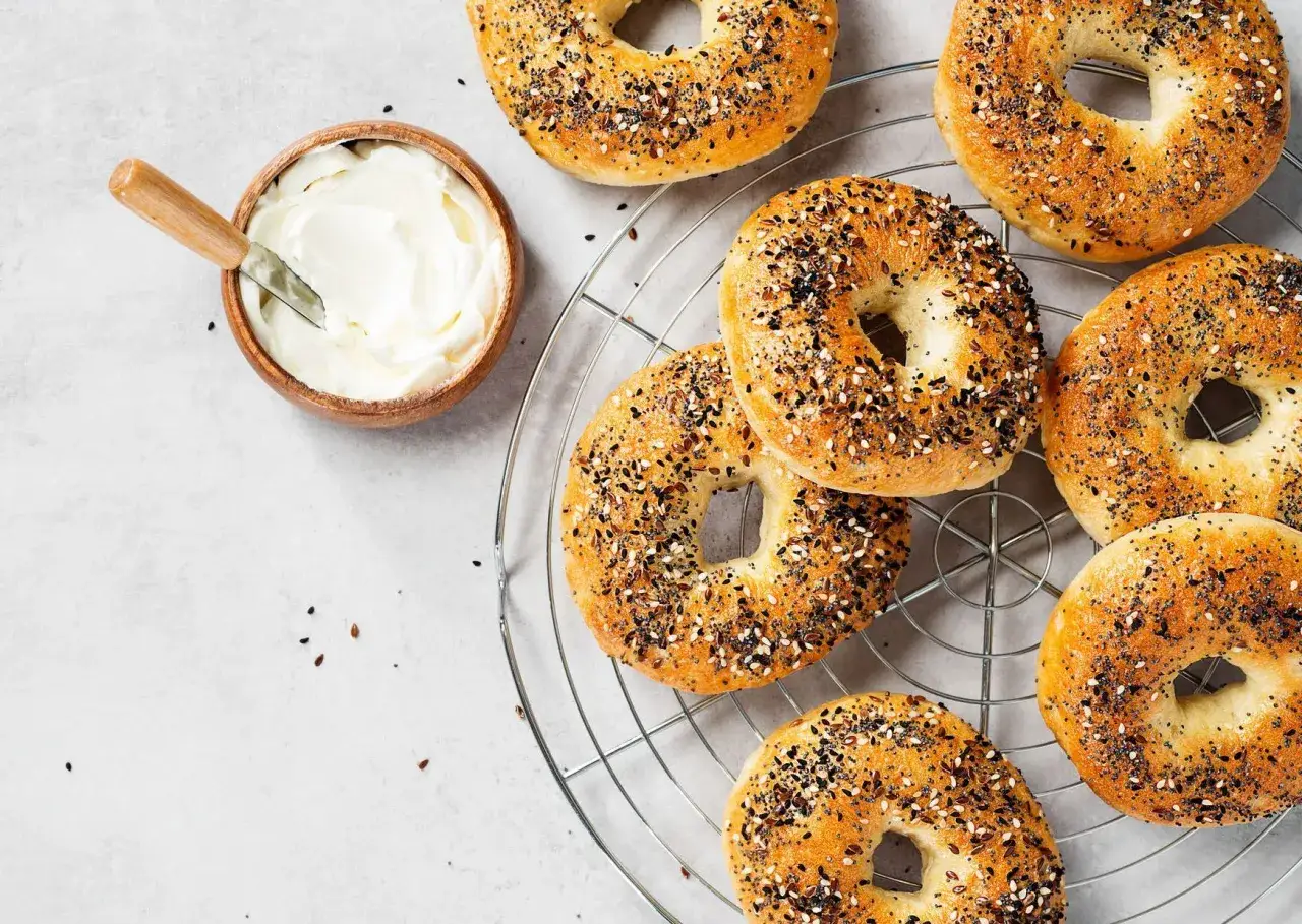 Bagels moelleux aux graines sur une grille, avec un bol de fromage &agrave; la cr&egrave;me. Parfait pour une recette facile et gourmande.